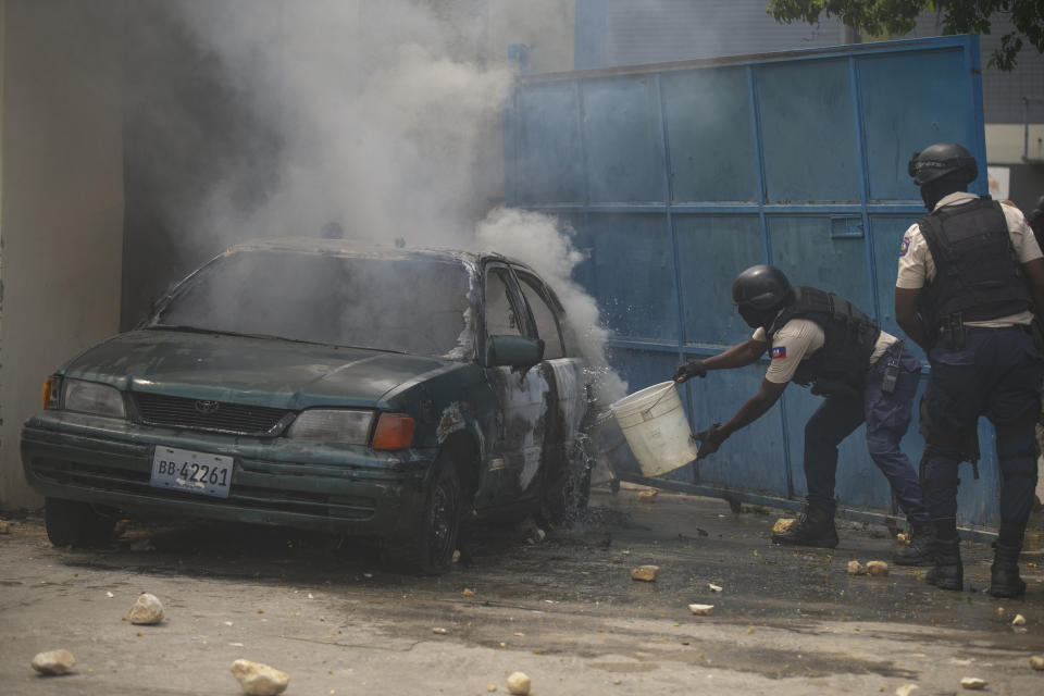 A police officer throws water on a burning vehicle in the parking of the police headquarters during a protest to demand the resignation of Prime Minister Ariel Henry in the Petion-Ville area of Port-au-Prince, Haiti, Monday, Oct. 3, 2022. (AP Photo/Odelyn Joseph)