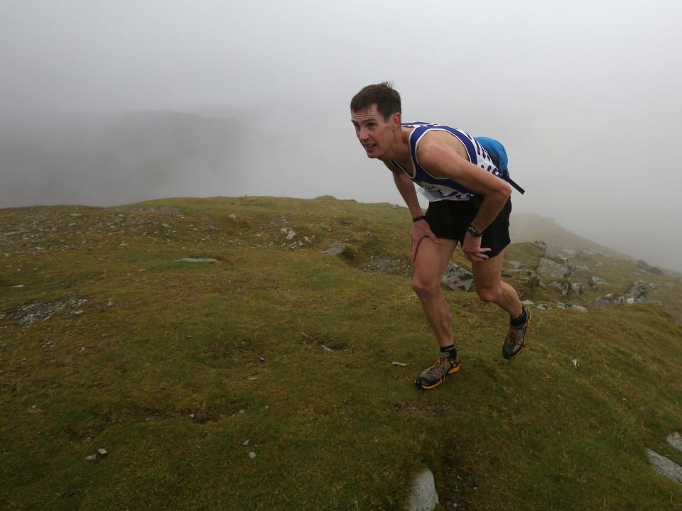 A person in blue athletic gear running up a mountain that is surrounded by fog.