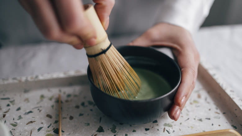 person frothing matcha with bamboo whisk