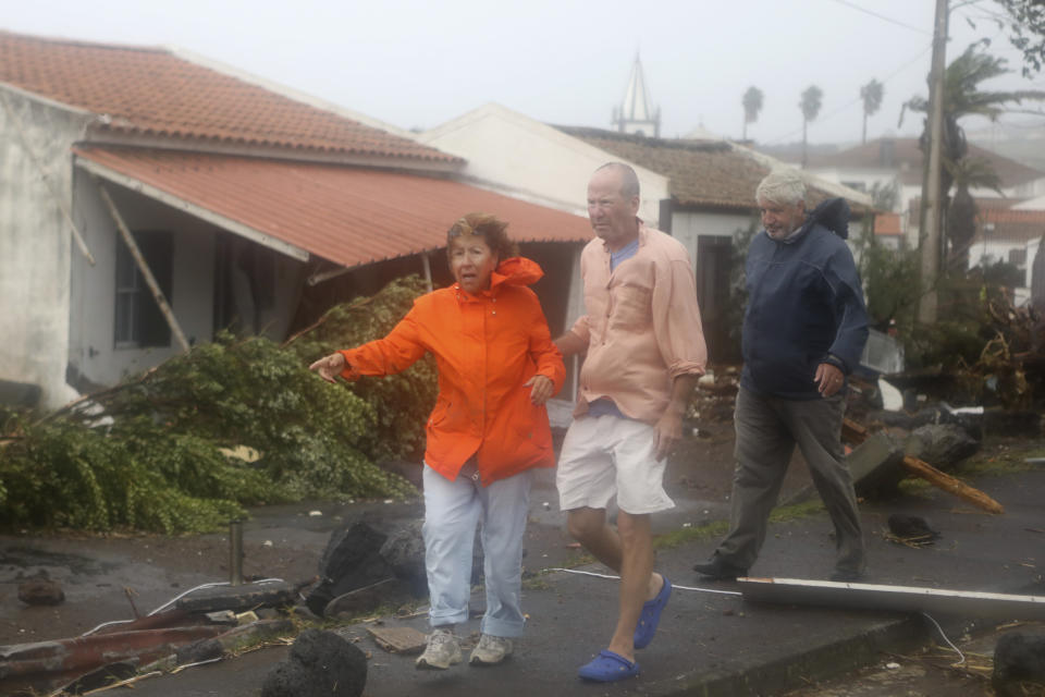 Don Marks, from Massachusetts in the US, center, and his wife Celeste walk among debris on their way to look at their wrecked seafront house in the village of Feteira, outside Horta, in the Portuguese island of Faial, Wednesday, Oct. 2, 2019. Hurricane Lorenzo is lashing the mid-Atlantic Azores Islands with heavy rain, powerful winds and high waves. The Category 2 hurricane passed the Portuguese island chain Wednesday. (AP Photo/Joao Henriques)