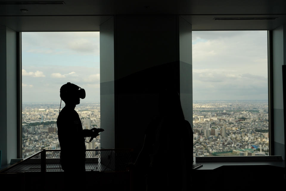 With a view of Tokyo's cityscape, a man wearing a VR headset plays a video game at the Sky Circus Sunshine 60 observatory Monday, Oct. 7, 2019, in Tokyo. (AP Photo/Jae C. Hong)