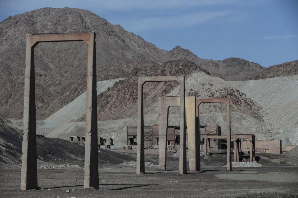 Iron structures led to a a rusted metal building with arid, rocky mountain above it.