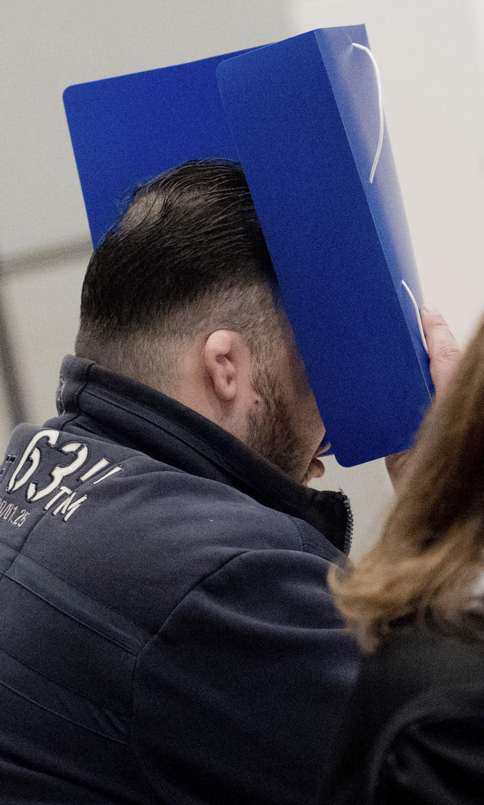 The defandant covers his face with a folder as he arrives at the temporay Oldenburg district court at the Weser Ems halls in Oldenburg, Germany, Tuesday, Oct. 30, 2018. The nurse serving a life sentence for two murders is going on trial on charges that he killed a further 100 patients at two hospitals in Germany. (Julian Stratenschulte/dpa via AP, Pool)