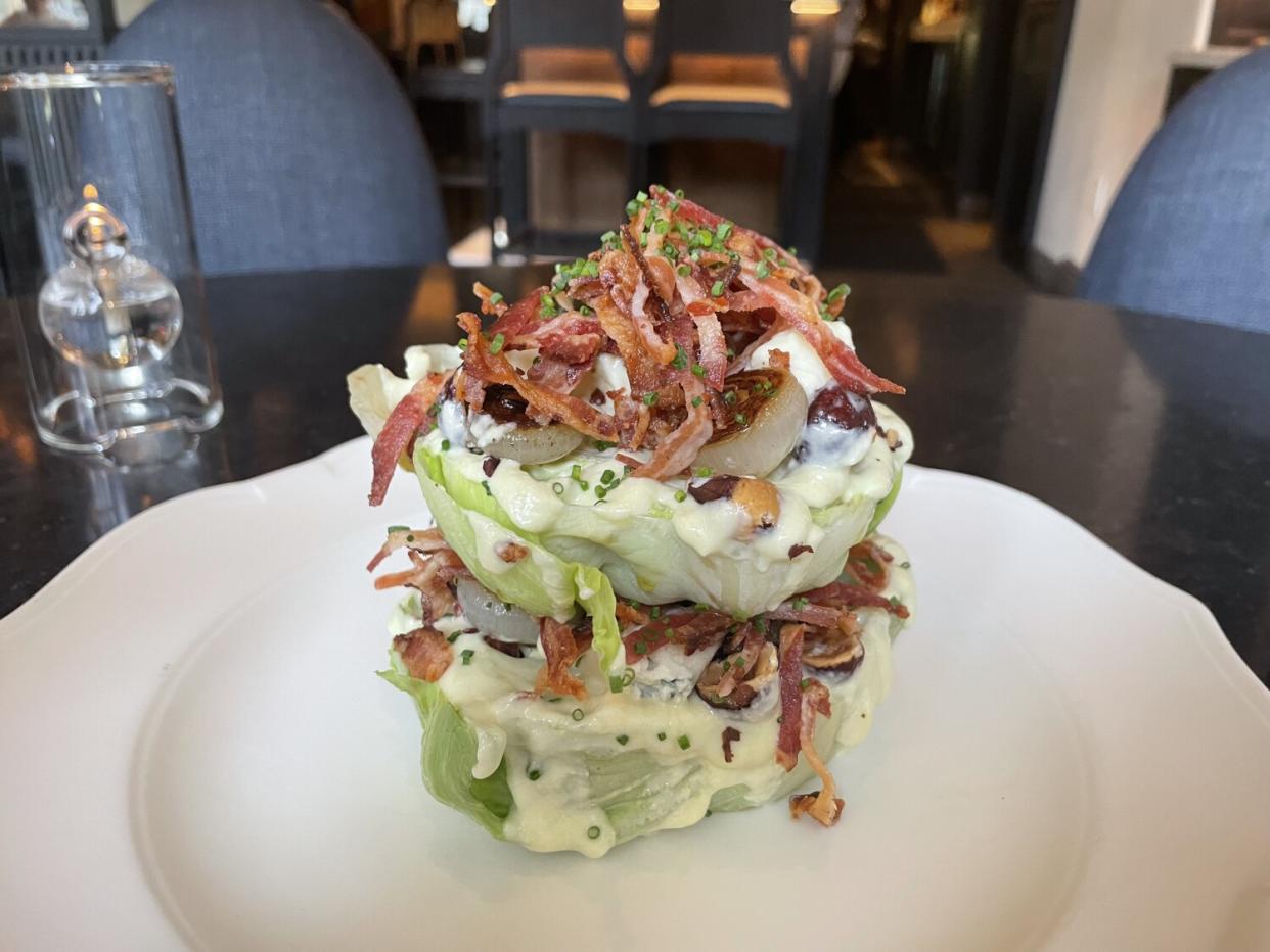 The wedge salad is a pile of lettuce with strips of bacon on a white plate.