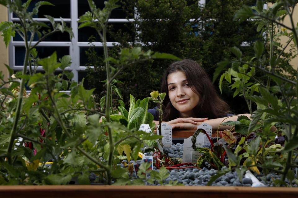 A young woman poses amid plants growing.