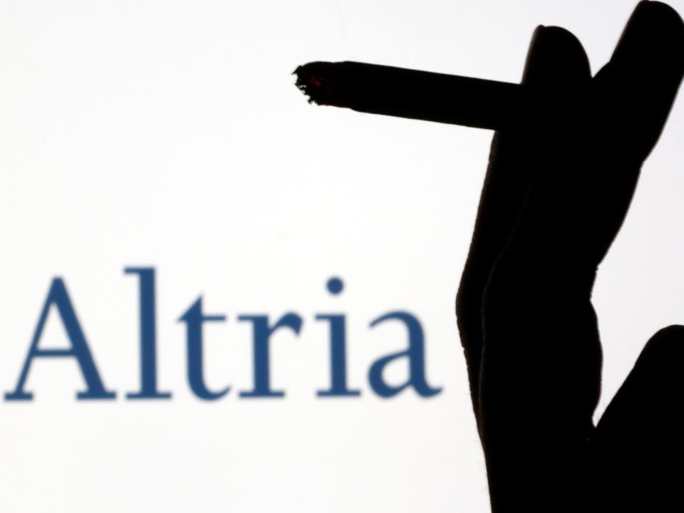 FILE PHOTO: A hand with a cigarette is seen in front of displayed logos of Philip Morris and Altria in this picture illustration taken September 26, 2019. REUTERS/Dado Ruvic/Illustration