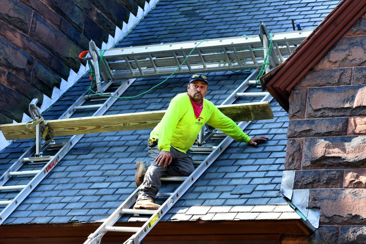 Otoniel Aguilar works to replace slate shingles on the roof of the Iglesia Adventista Central Church on Main South Wednesday.