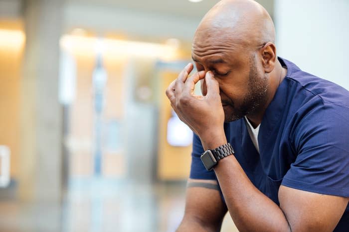 Person in scrubs appearing stressed with hand on forehead