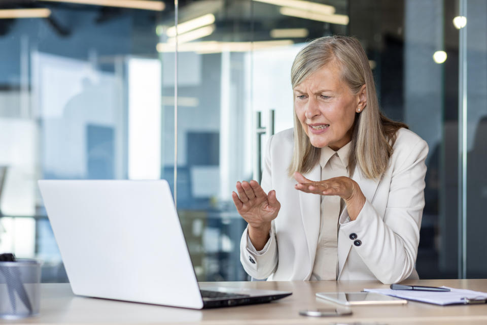 A frustrated woman gestures at a laptop screen during a meeting