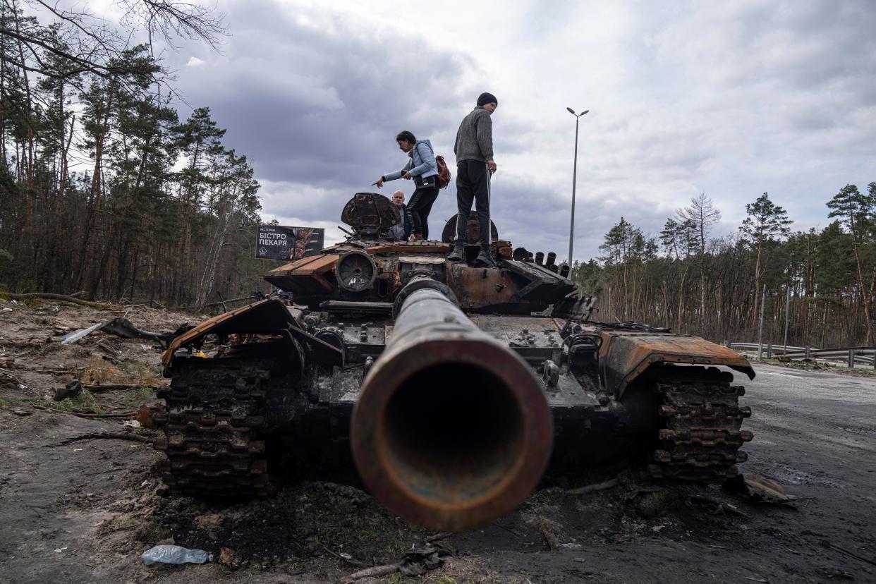 Residents on Monday stand atop of a Russian tank damaged during fighting between Russian and Ukrainian forces in the outskirts of Kyiv, Ukraine.