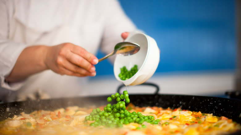 Cook pouring green peppercorns into pan of food