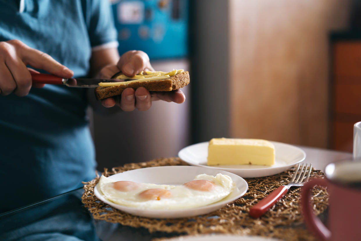 A man preparing homemade fried eggs for breakfast, spreading butter on bread. Cooking at home during quarantine