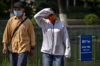 People wearing face masks walk past a sign reading "Mask on and stay away from crowds" at a green space in Beijing, Tuesday, May 17, 2022. (AP Photo/Mark Schiefelbein)