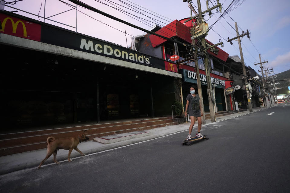 A woman surf skates past closed businesses along the normally tourist-packed Bangla walking street of Patong Beach on Phuket, southern Thailand, June 28, 2021. Thailand's government will begin the "Phuket Sandbox" scheme to bring the tourists back to Phuket starting July 1. Even though coronavirus numbers are again rising around the rest of Thailand and prompting new lockdown measures, officials say there's too much at stake not to forge ahead with the plan to reopen the island to fully-vaccinated travelers. (AP Photo/Sakchai Lalit)