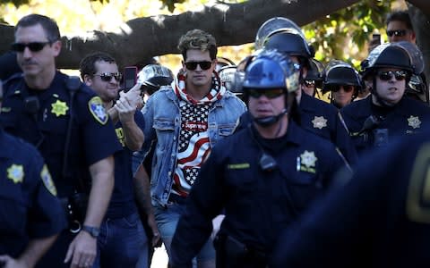 Right wing commentator Milo Yiannopoulos is escorted by police officers after he spoke during a free speech rally at U.C. Berkeley in September - Credit: Getty
