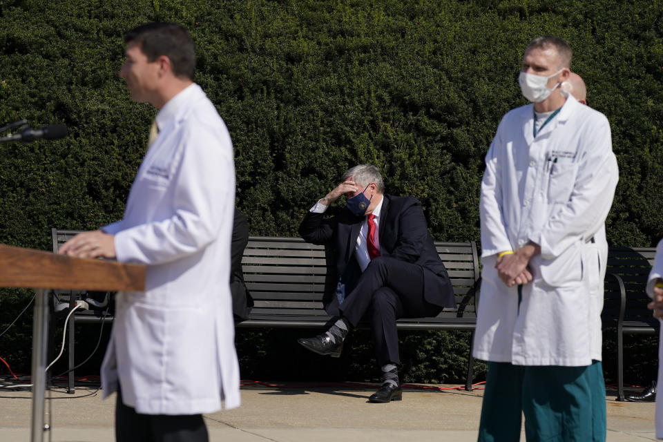 El jefe de despacho de la Casa Blanca Staff Mark Meadows (sentado, al centro) escucha mientras el médico del presidente Donald Trump, el doctor Sean Conley, habla frente a los reporteros frente al Centro Médico Militar Nacional Walter Reed, en Bethesda, Maryland, el domingo 4 de octubre de 2020. Trump pasó su segunda noche en ese hospital tras caer enfermo de coronavirus. (AP Foto/Jacquelyn Martin)