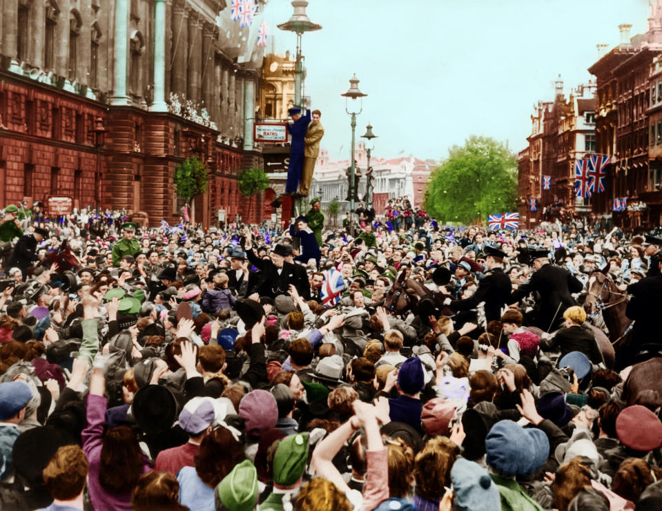 Wartime PM Winston Churchill raising up and giving his famous V for Victory sign, joining the huge crowd celebrating near Whitehall in London.