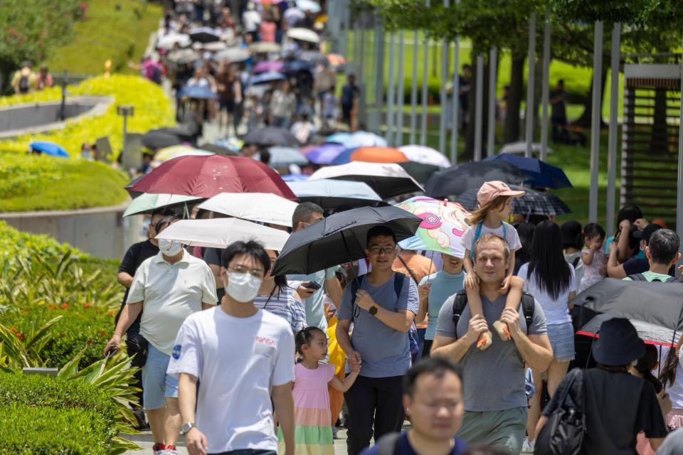 People walking with umbrellas in Hong Kong on sunny day.