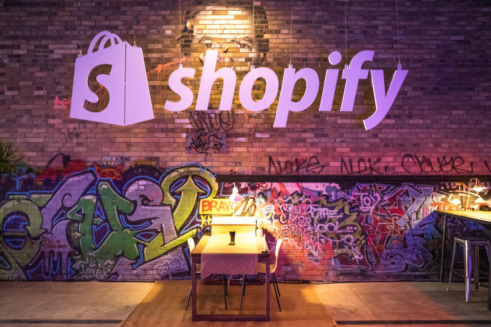 A small table lit by a reading lamp in front of a graffiti strewn wall, with the Shopify logo hanging overhead.