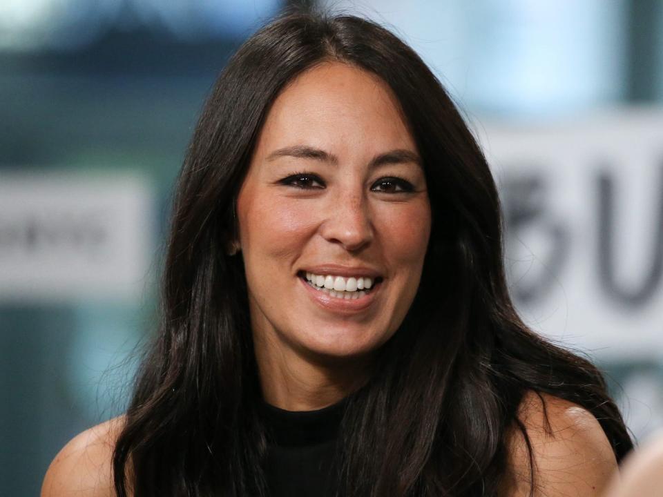Joanna Gaines smiles in front of a blue backdrop.