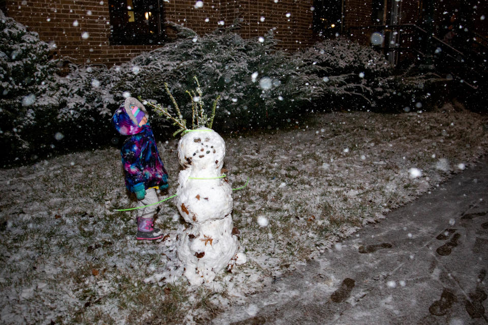 A child stands next to a snowman made during the Zeeland Magical Christmas Parade on Monday, Nov. 29, 2021.