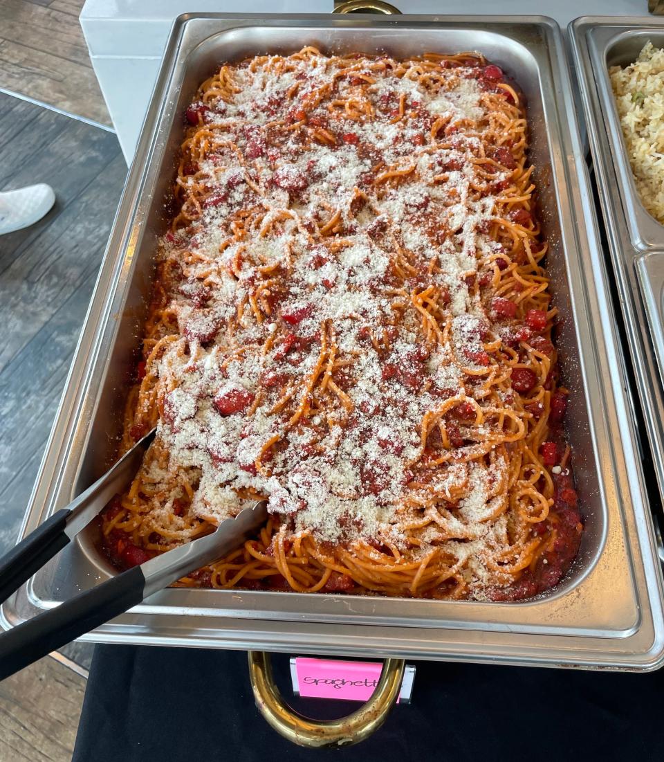 A large, silver tray filled with spaghetti covered in tomato sauce and sprinkled with grated cheese, with serving tongs on the side