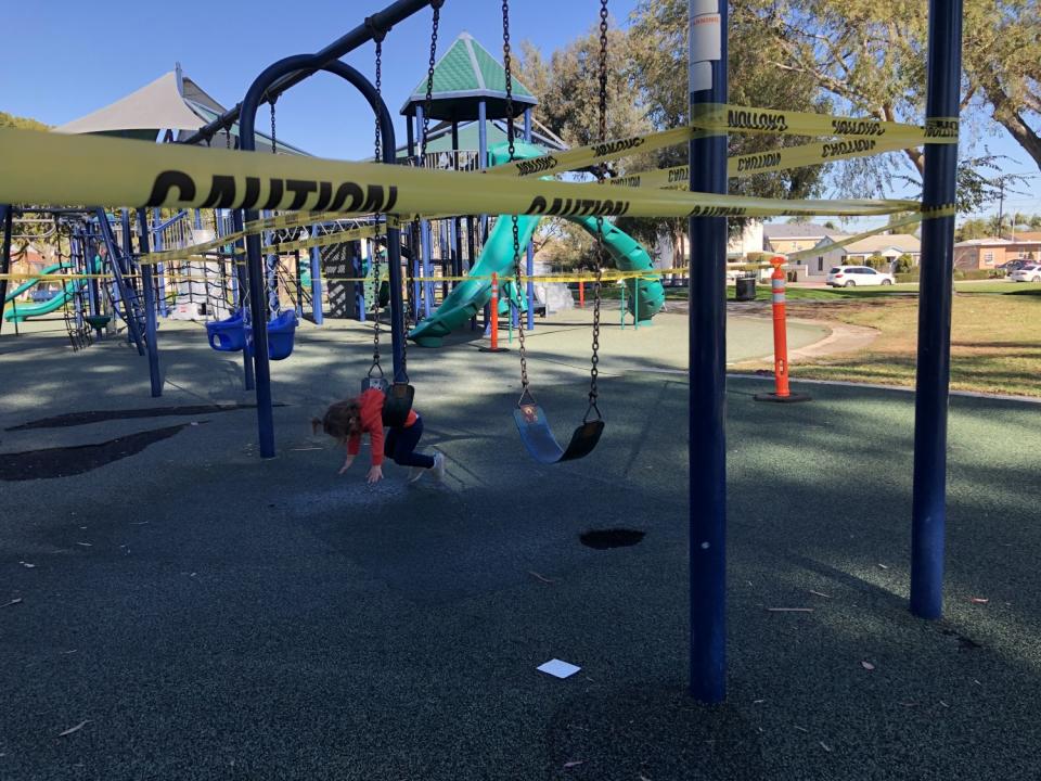 An infant plays on a swing at a playground that is taped off