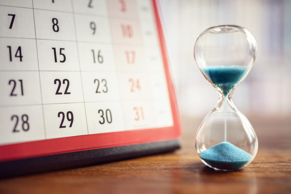 A half-emptied hourglass next to a calendar on a table.