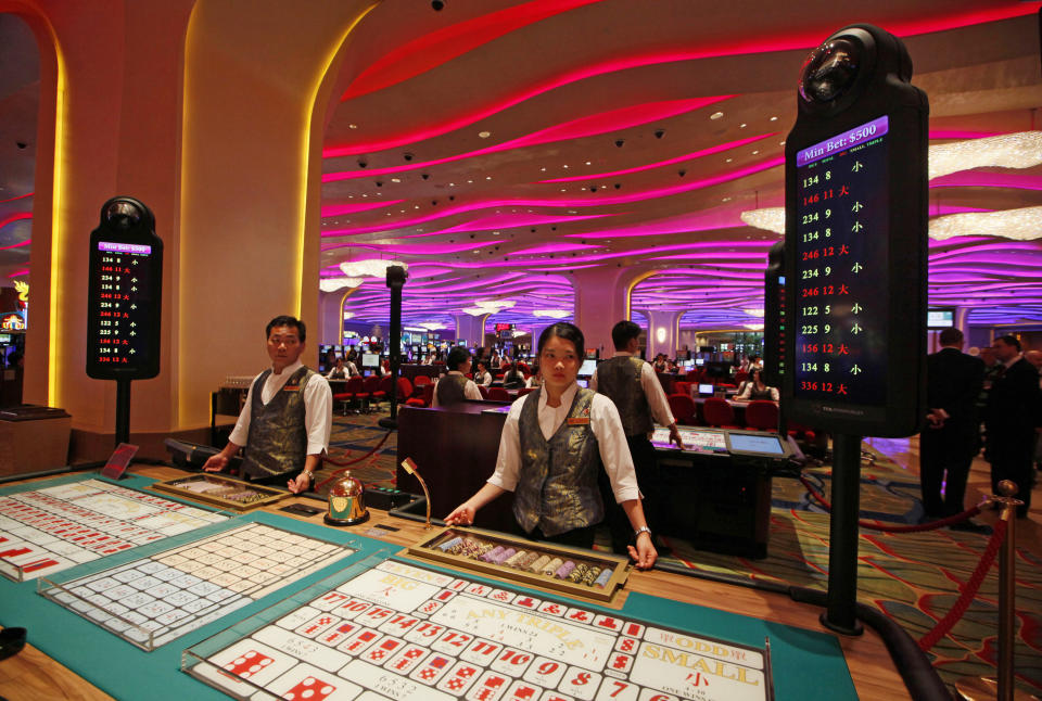 FILE - Croupiers stand at a Sic Bo gaming table inside a casino at the Sands Cotai Central in Macao on Sept. 20, 2012. The Asian gambling center of Macao will close all its casinos for a week starting Monday, July 11, and largely restrict people to their homes as it tries to stop a COVID-19 outbreak that has infected more than 1,400 people in the past three weeks. (AP Photo/Kin Cheung, File)