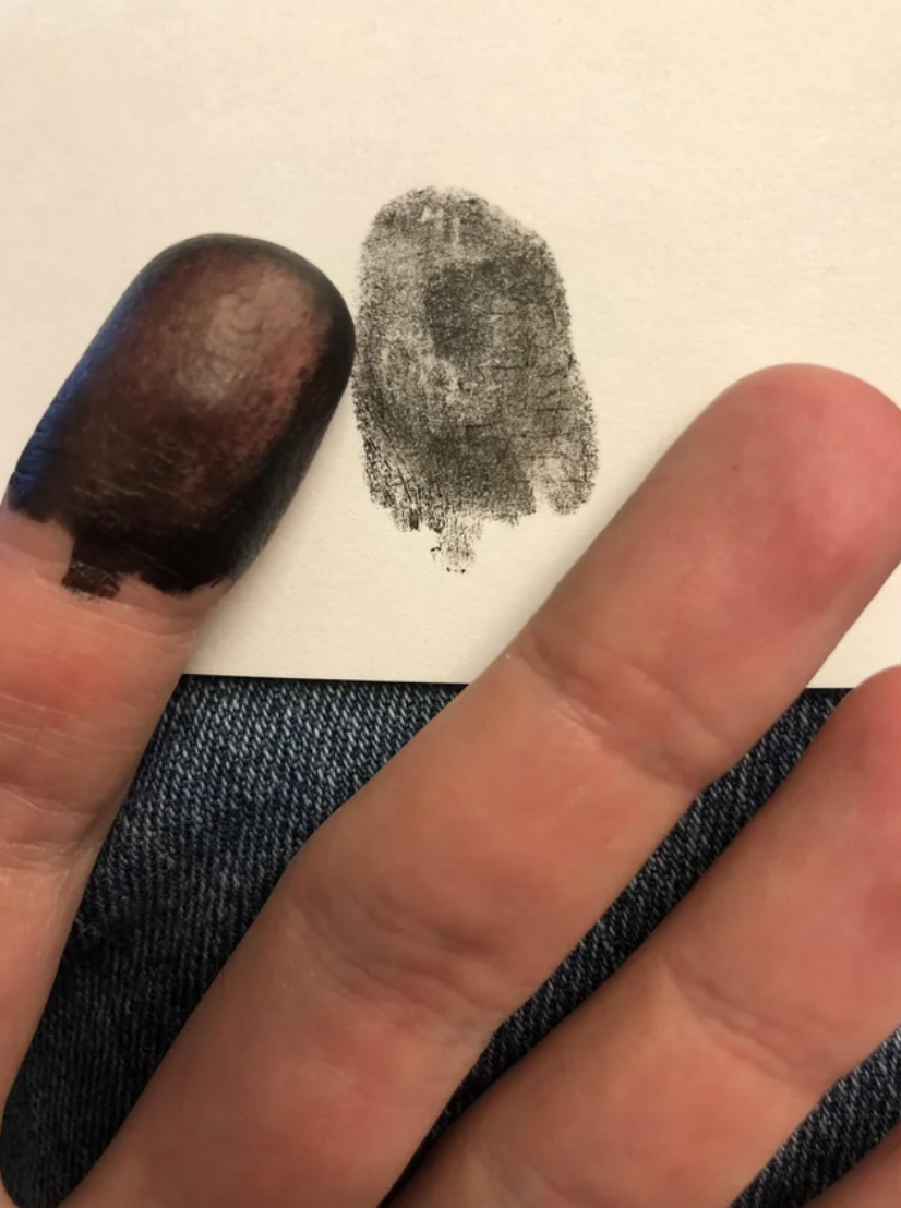 Fingerprint next to a thumbprint smudge on paper, held by a person's hand