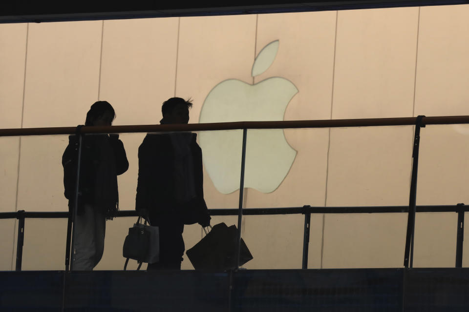 FILE - In this Jan. 3, 2019, file photo, shoppers pass by the Apple store logo at a shopping mall in Beijing. Apple Inc. reports financial results Tuesday, April 30. (AP Photo/Ng Han Guan, File)