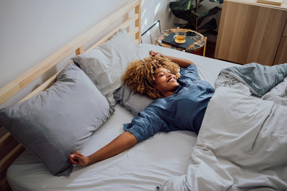 Woman is lying in her bed in the morning. She is stretching and smiling.