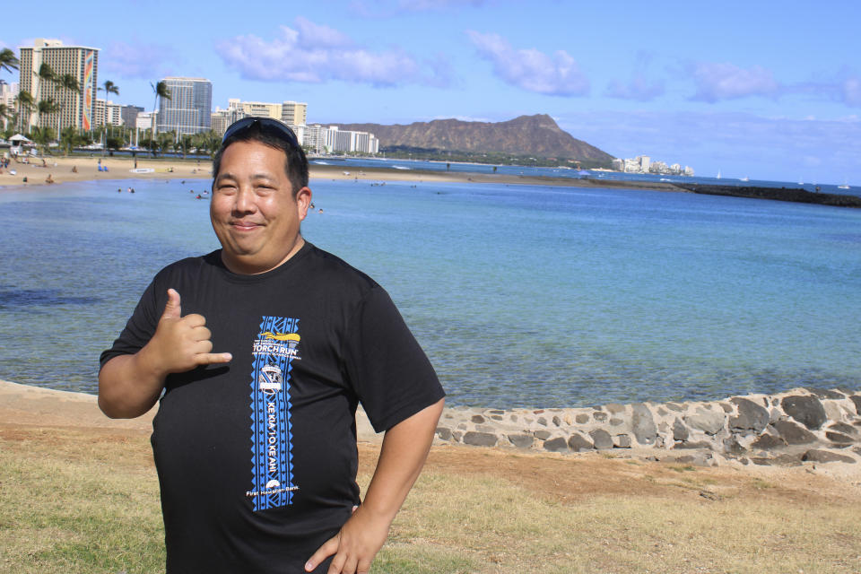 CORRECTS SPELLING OF LAST NAME TO YUKUTAKE- NOT YAKUTAKE- Todd Yukutake, a director of the Hawaii Firearms Coalition, stops to pose in front of Diamond Head while taking a walk through a beach park in Honolulu, Thursday June 29, 2023. The coalition is suing to block a new Hawaii law that prohibits carrying guns in sensitive locations including parks and beaches. Beginning Saturday, JUly 1, 2023, a new law prohibits carrying a firearm on the sand — and in other places, including banks, bars and restaurants that serve alcohol. (AP Photo/Jennifer Sinco Kelleher)