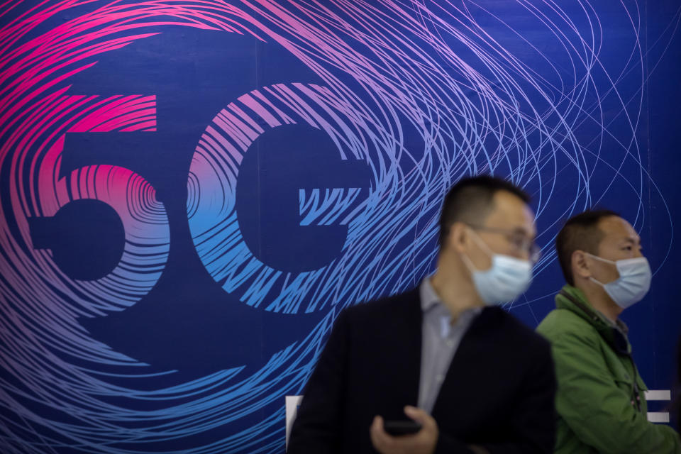 People wearing face masks to protect against the spread of the coronavirus walk past a display advertising 5G wireless services at the PT Expo in Beijing, Wednesday, Oct. 14, 2020. Chinese leaders are shifting focus from the coronavirus back to long-term goals of making China a technology leader at this year's highest-profile political event, the meeting of its ceremonial legislature, amid tension with Washington and Europe over trade, Hong Kong and human rights. (AP Photo/Mark Schiefelbein)