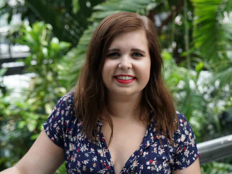 Samantha Reid, a white woman with brown hair, poses in front of green plants.