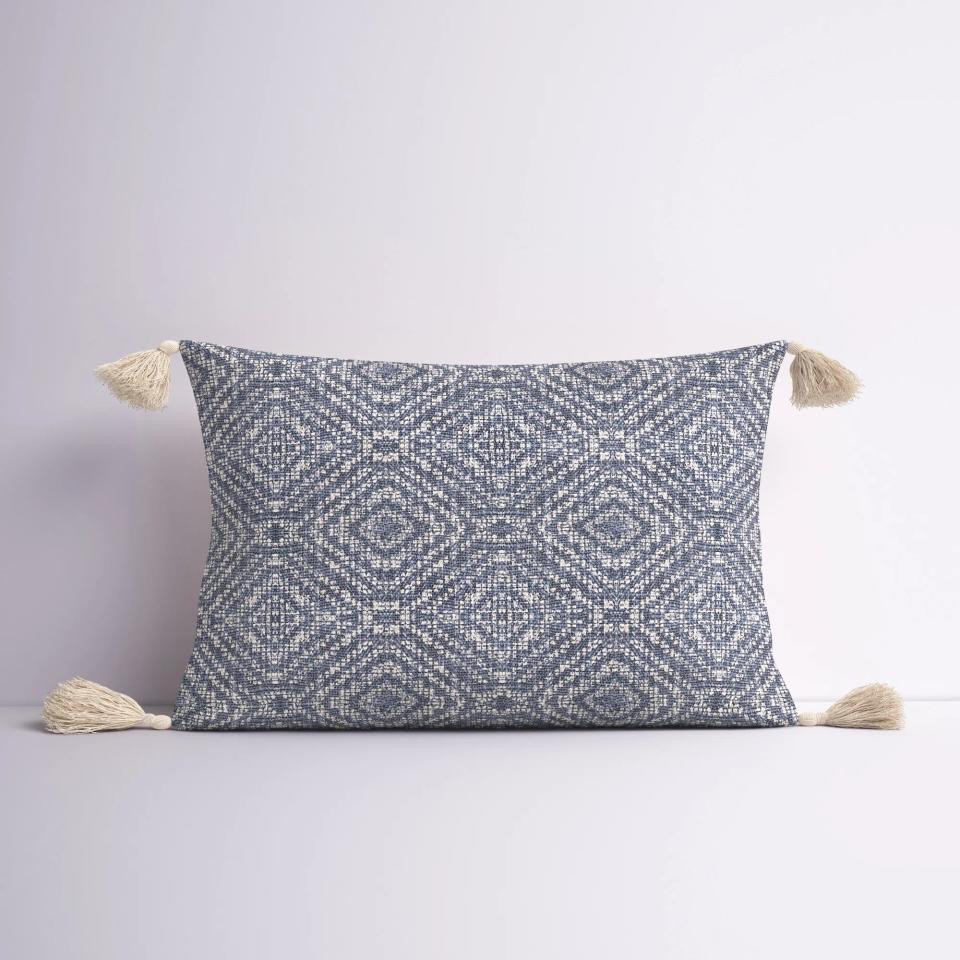 The pillow with a blue and white geometric pattern and a tassel on each corner