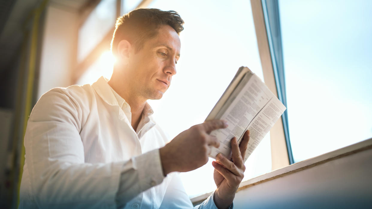 Low angle view of a mid adult doctor reading a book by the window.