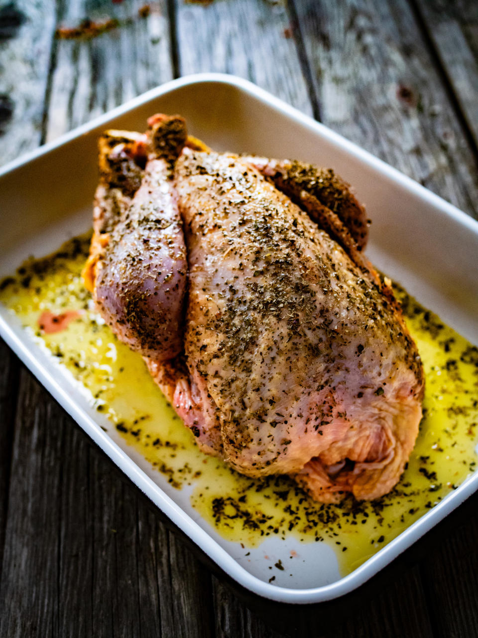 Raw whole chicken rubbed with spices in cooking pan on wooden table