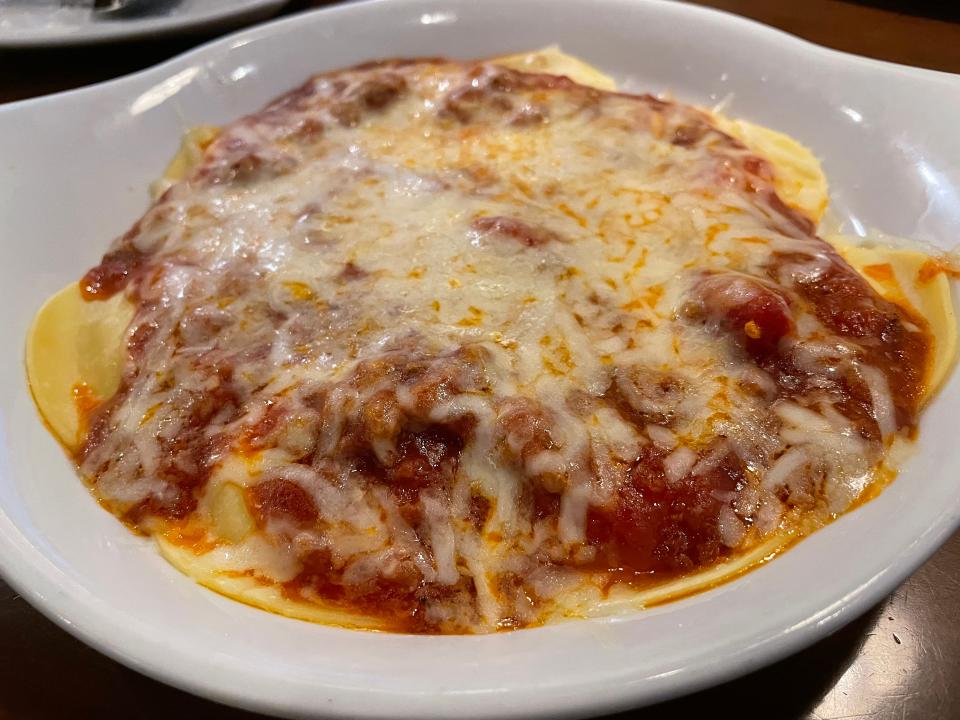 Large plate of ravioli with tomato sauce and melted cheese on top served in a white bowl