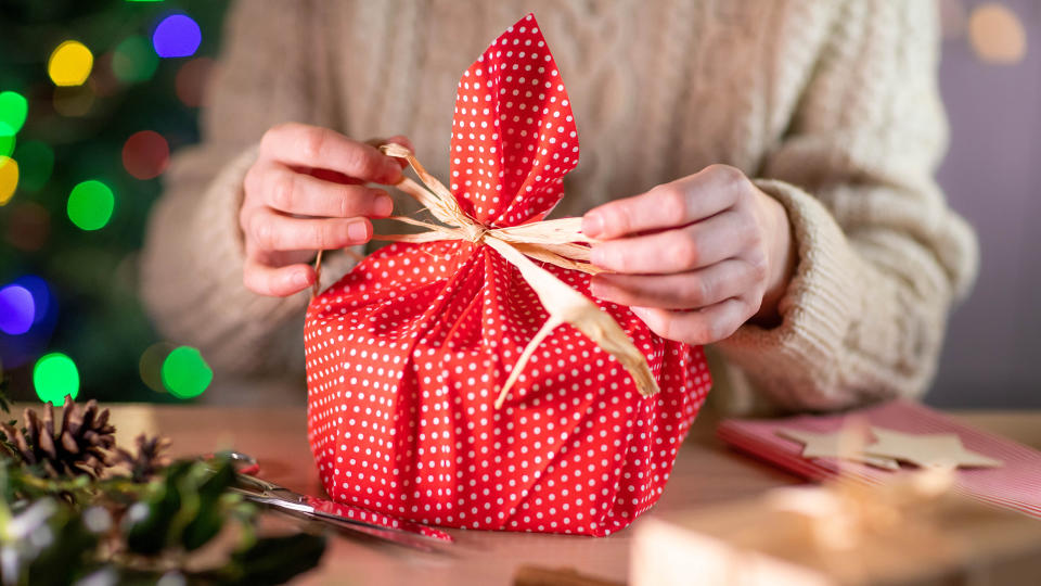 Woman wrapping a Christmas gift in red and gold spotted cloth, tied with a gold ribbon