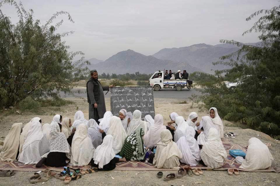 Afghan refugees pass by an outdoor girls classroom in Torkham, Afghanistan, Saturday, Nov. 18, 2023. Many Afghan refugees arrived at the Torkham border with Pakistan to return home shortly before the expiration of a Pakistani government deadline for those who are in the country illegally, or face deportation. (AP Photo/Ebrahim Noroozi)