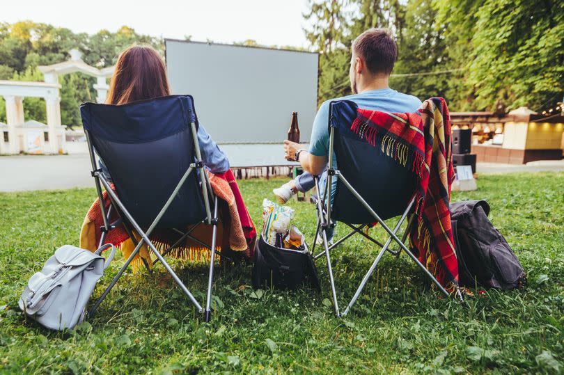 couple sitting in camp-chairs in city park looking movie outdoors at open air cinema lifestyle