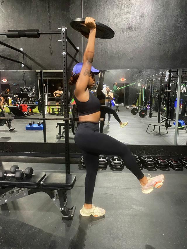 The author holding a weighted plate over her head while doing a single leg squat.
