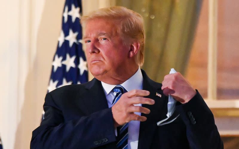 U.S. President Donald Trump pulls off his face mask as he returns to the White House after being hospitalized at Walter Reed Medical Center for coronavirus disease (COVID-19), in Washington