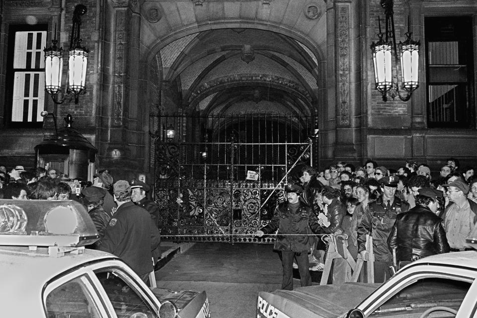 FILE - In this Dec. 9, 1980, file photo, a crowd gathers outside the Dakota apartment building after John Lennon, who lived there, was shot hours earlier in front of the building when returning home on the evening of Dec. 8. Mark David Chapman, who shot and killed Lennon, said he was seeking glory and deserved the death penalty for the "despicable" act. Chapman made the comments in response to questions last month from a parole board, which denied him parole for an 11th time. (AP Photo/Ray Stubblebine, File)