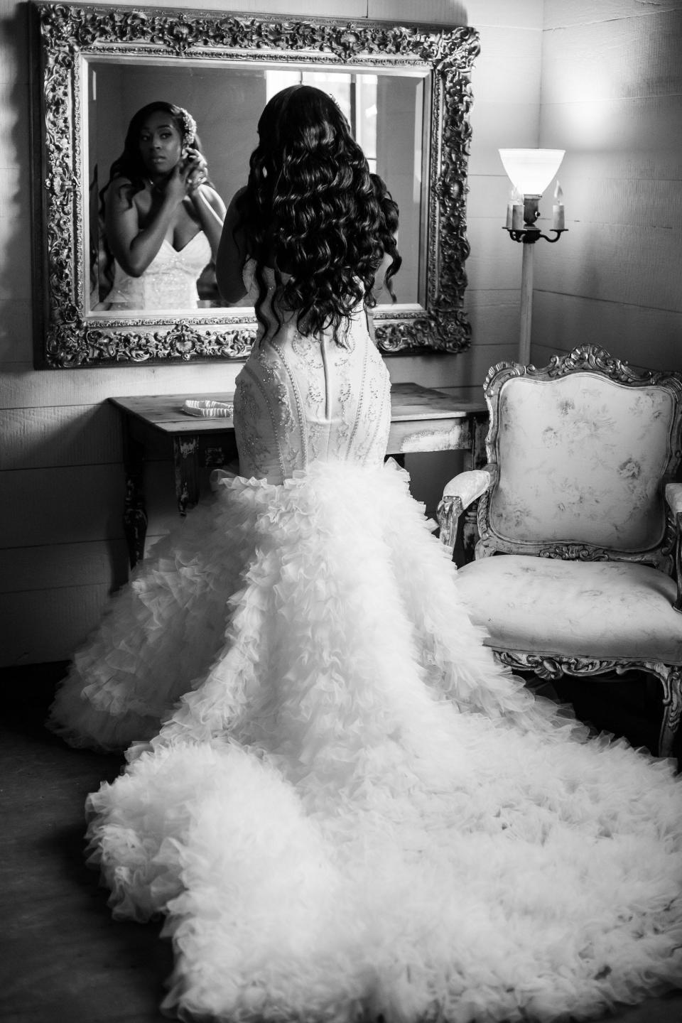 A bride puts on her earrings and looks in a mirror while wearing her wedding dress.