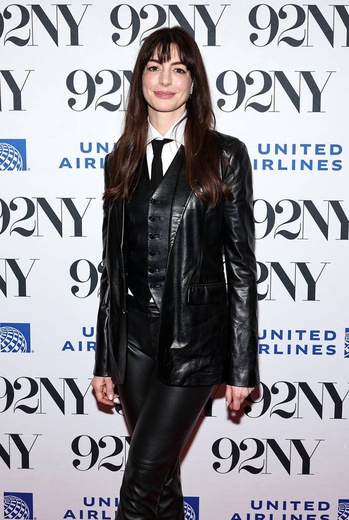 Anne Hathaway poses in a sleek black leather suit, white shirt, and tie at a 92NY and United Airlines event