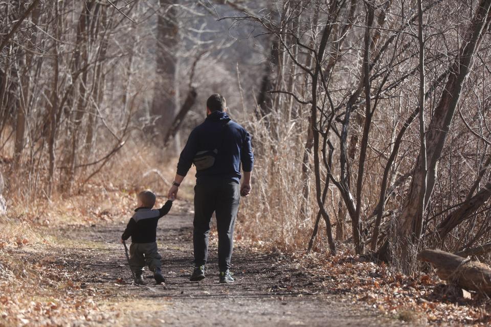 A father and child walk along a trail in Mendon Ponds Park in Pittsford.  Warmer temperatures have had people shedding their winter coats.