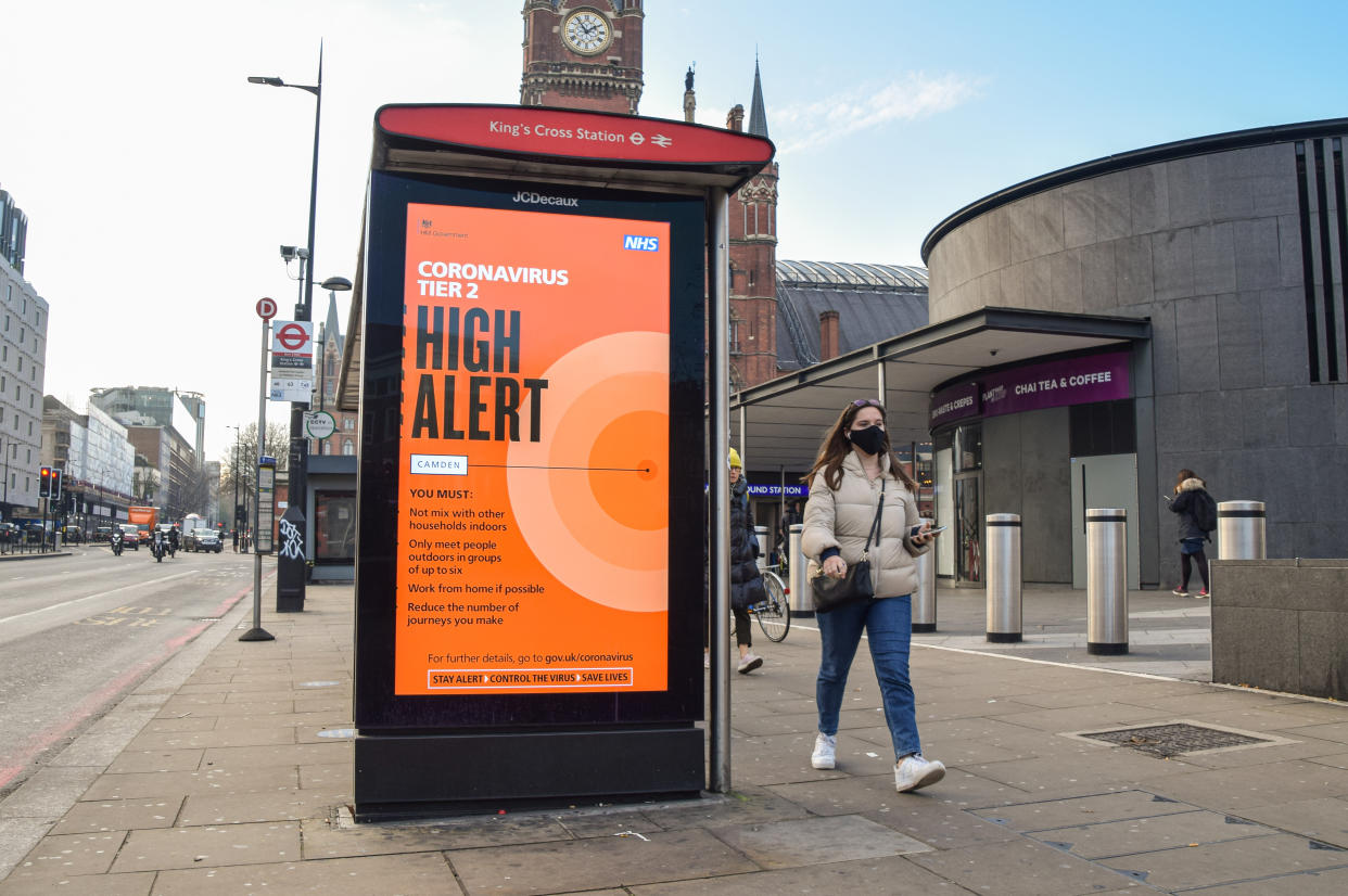 LONDON, UNITED KINGDOM - 2020/12/08: A woman wearing a protective mask walks past a Coronavirus High Alert information poster in King's Cross. England has imposed a three-tier system of restrictions, with London currently in Tier 2: High. (Photo by Vuk Valcic/SOPA Images/LightRocket via Getty Images)