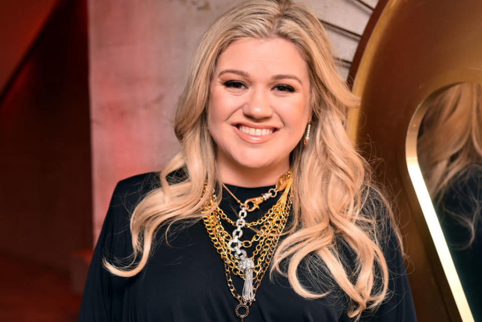 Kelly at a Pre-Grammy event, her hair is blonde and she wears a blouse with layers of chain necklaces